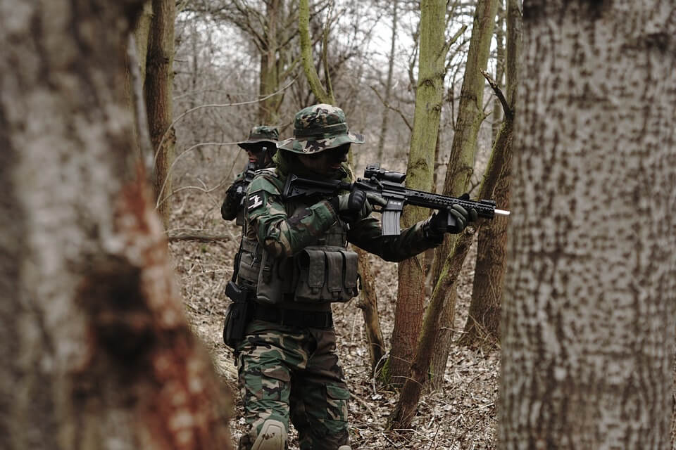 Two people in military clothing playing airsoft in a forest